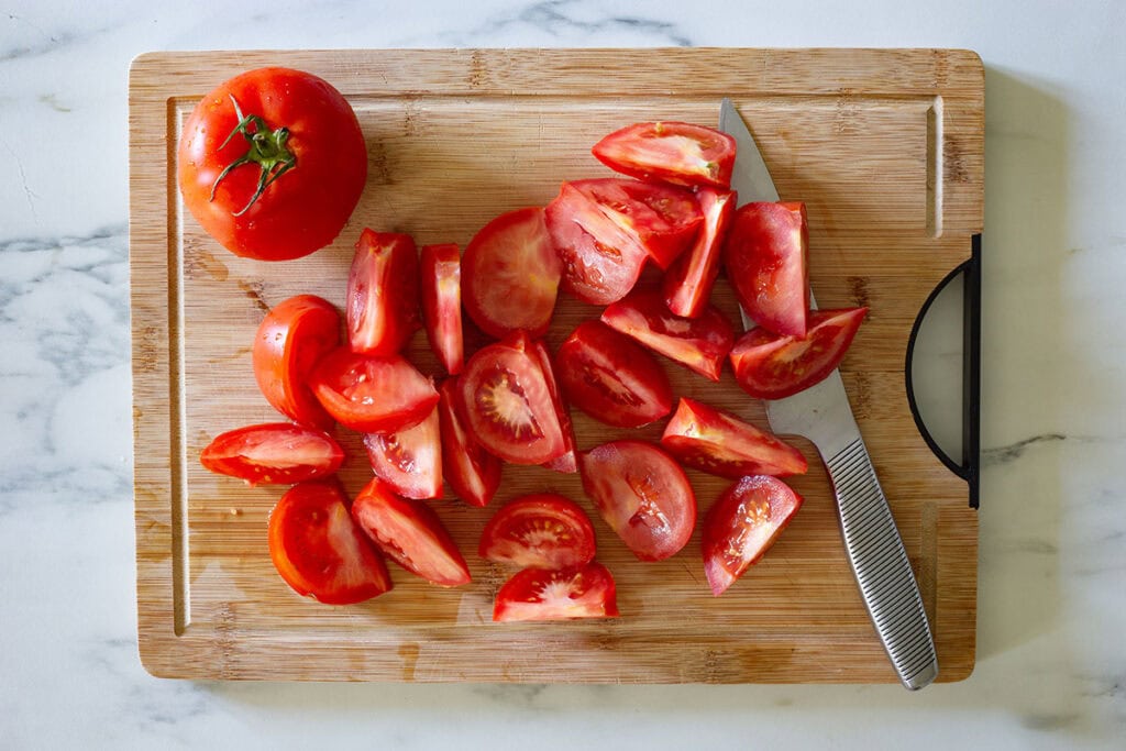 Tomatoes cut into wedges on a cutting board.