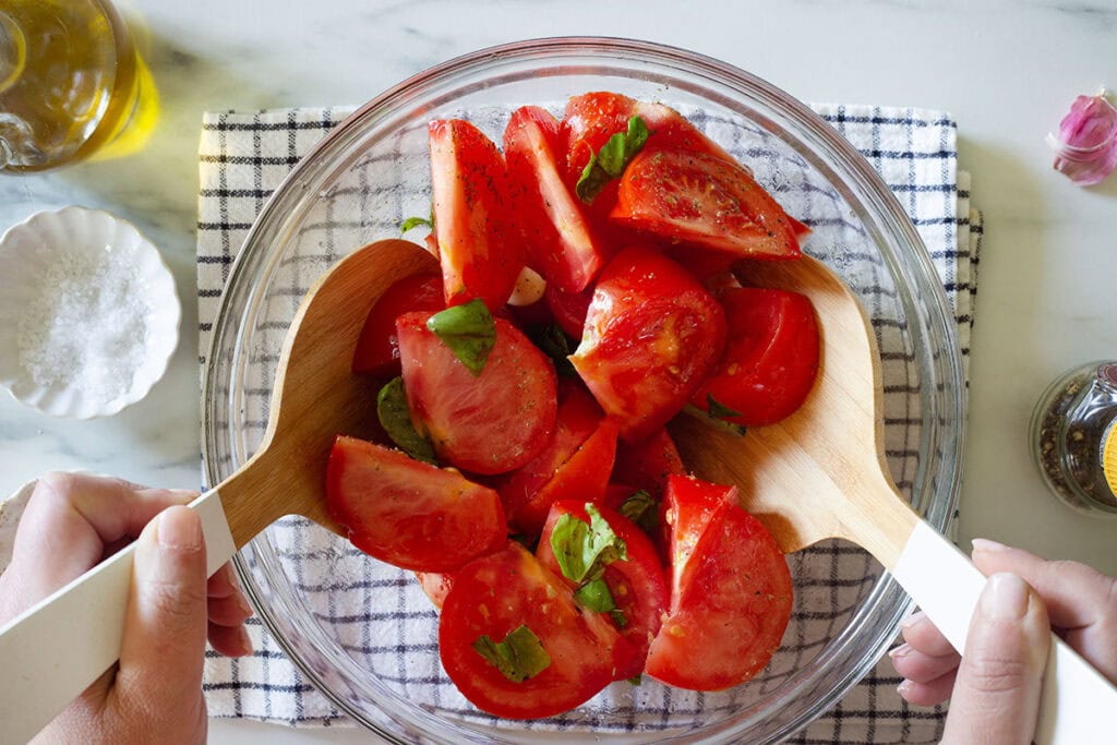 Two hands mixing the ingredients for the tomato salad in a bowl.