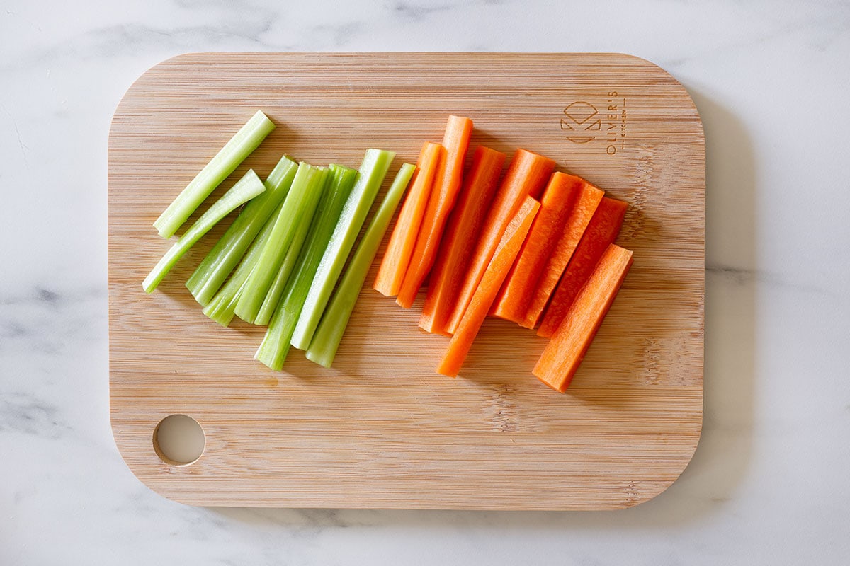Celery and carrot cut into small sticks on a cutting board.