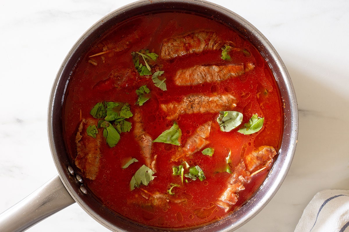 The small roulades simmering in tomato sauce with a few basil leaves.