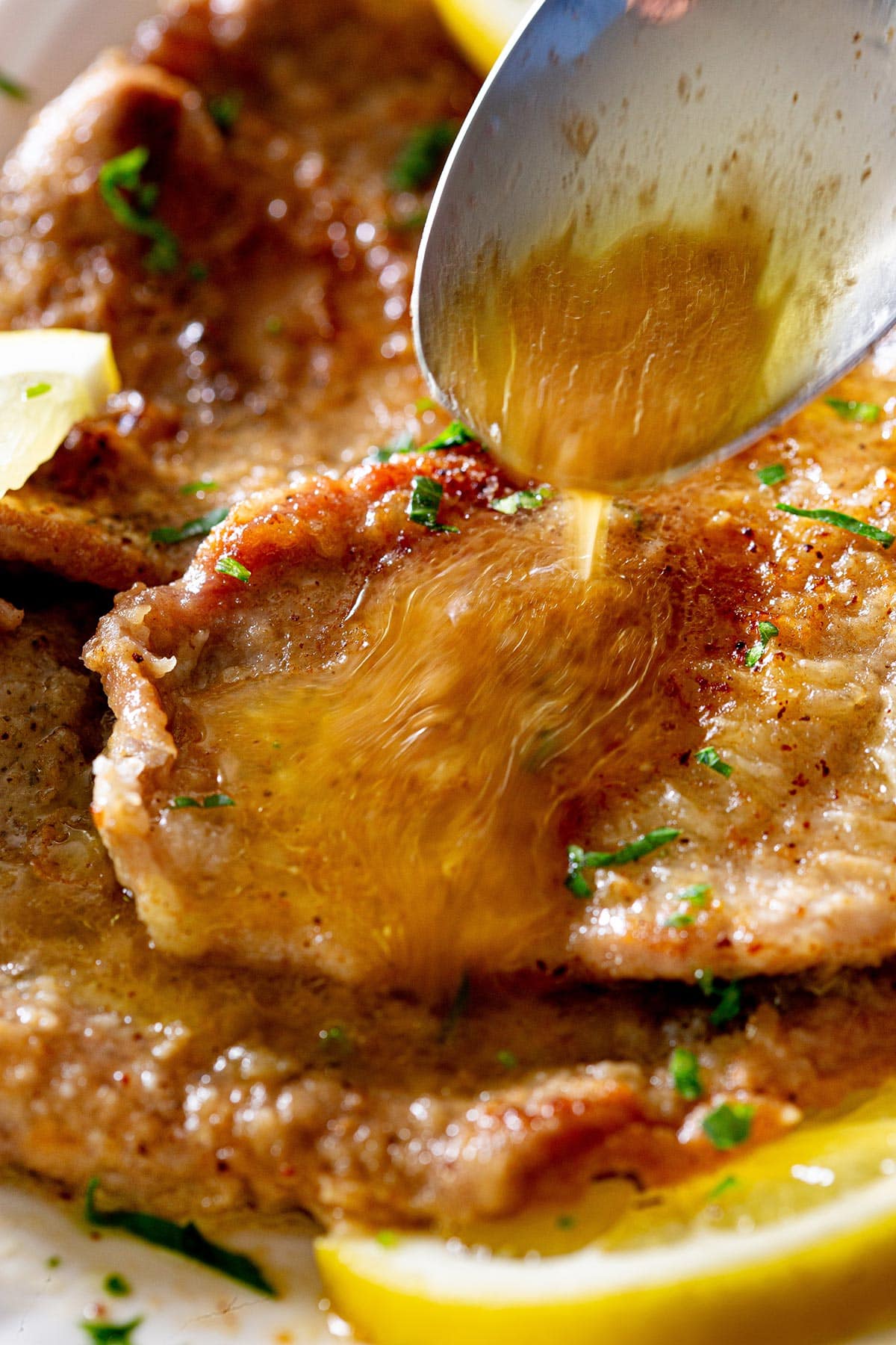 Close-up of spooning the lemony sauce over a scaloppine.