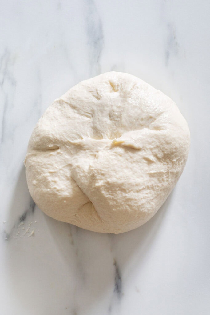 The dough stretched and shaped in a ball on a kitchen surface.