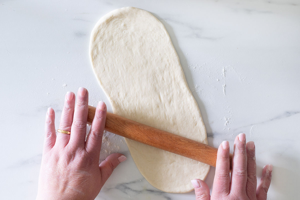 Rolling a piece of dough into an oval shape.