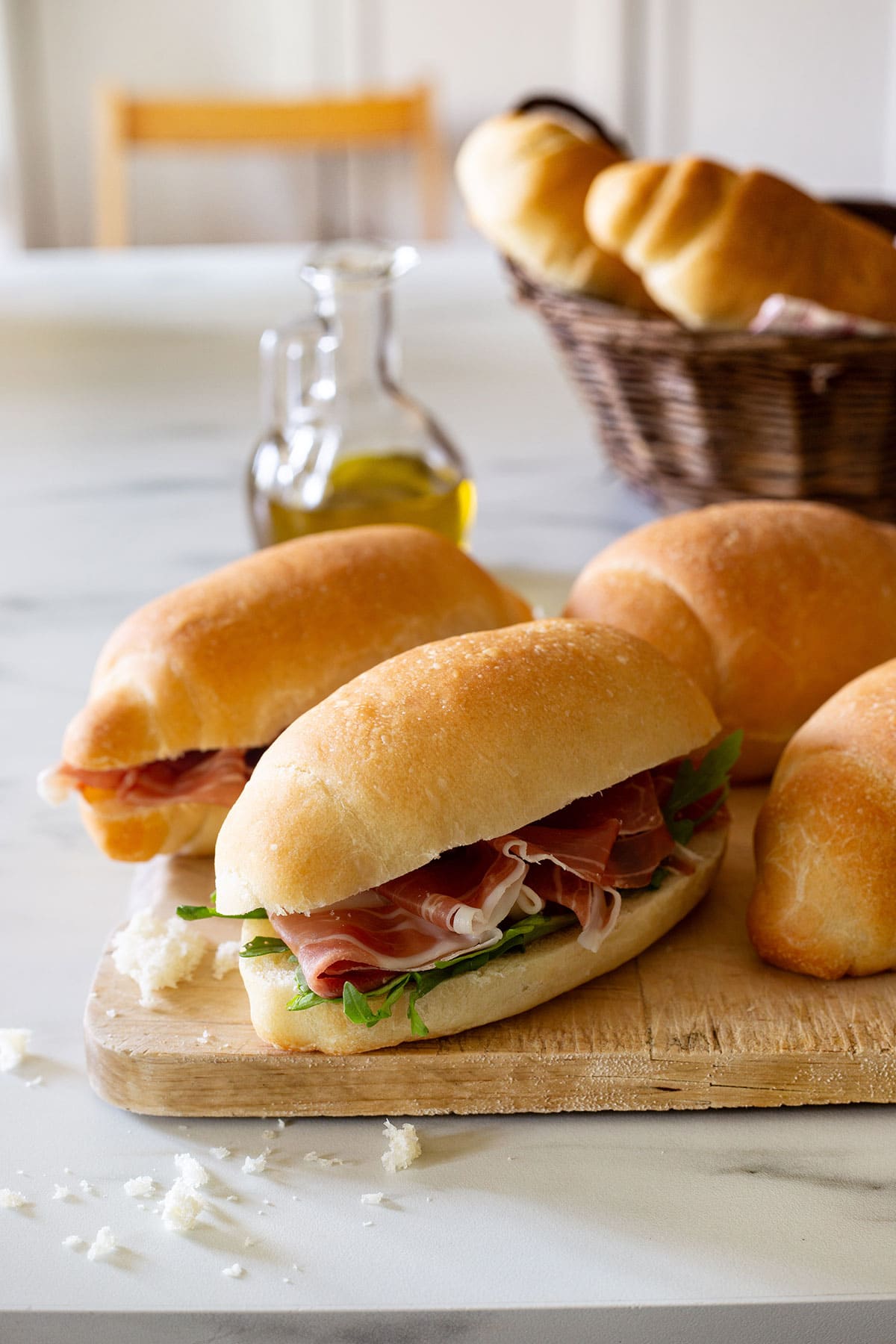 Panini all'olio rolls stuffed with prosciutto and arugula, placed on a cutting board.