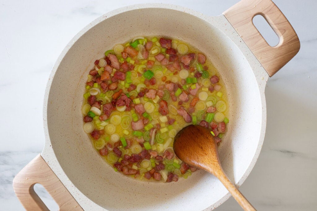 Bacon and green onions sautéing in a pot.
