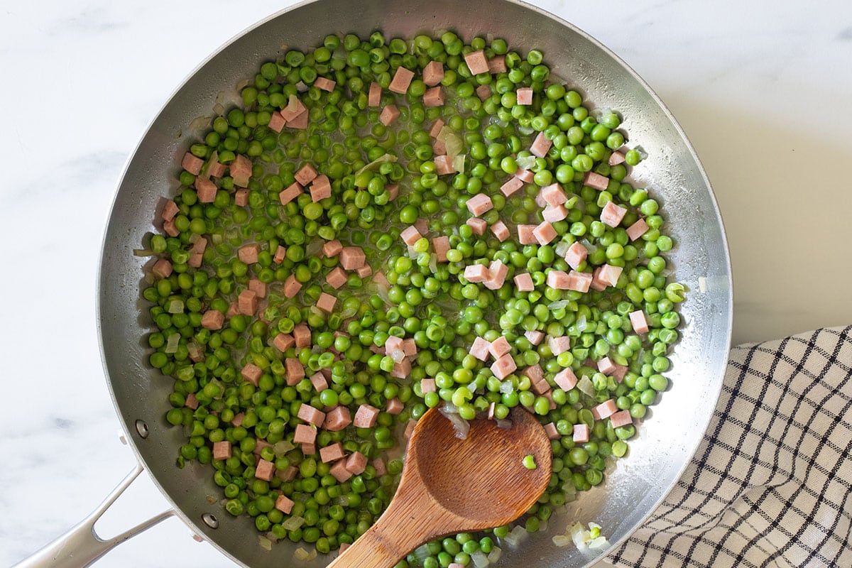 Fully cooked piselli e prosciutto in a pan.