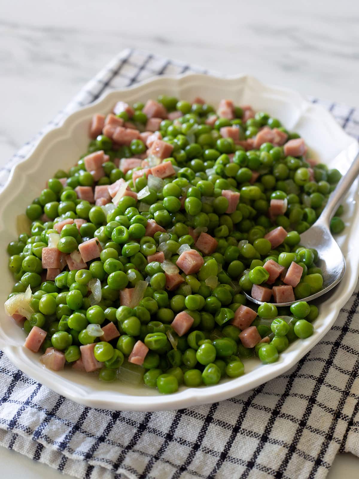 Piselli e prosciutto in a serving platter.