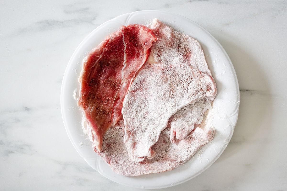 Veal slices floured on a plate.