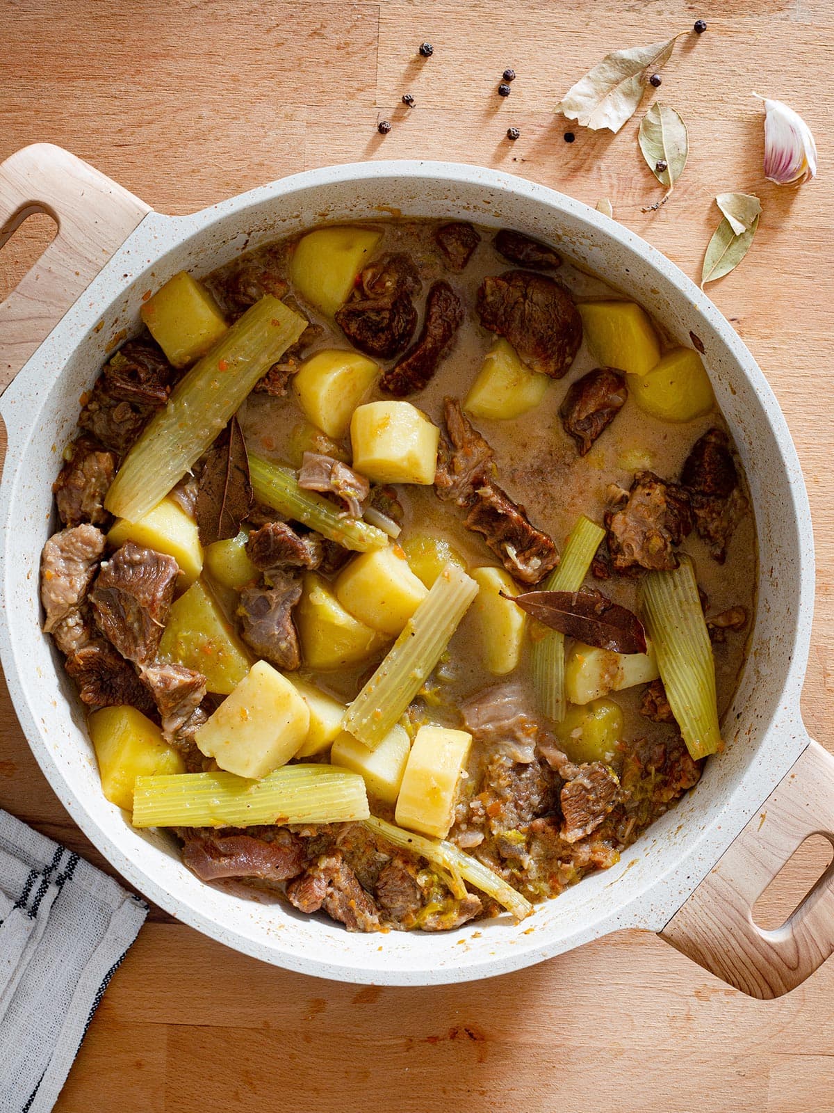 Spezzatino di manzo in a braising pan and some spices and herbs scattered around.