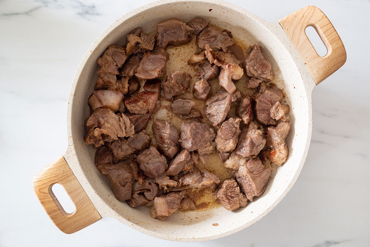 Beef chunks cooked until brown in a braising pan.