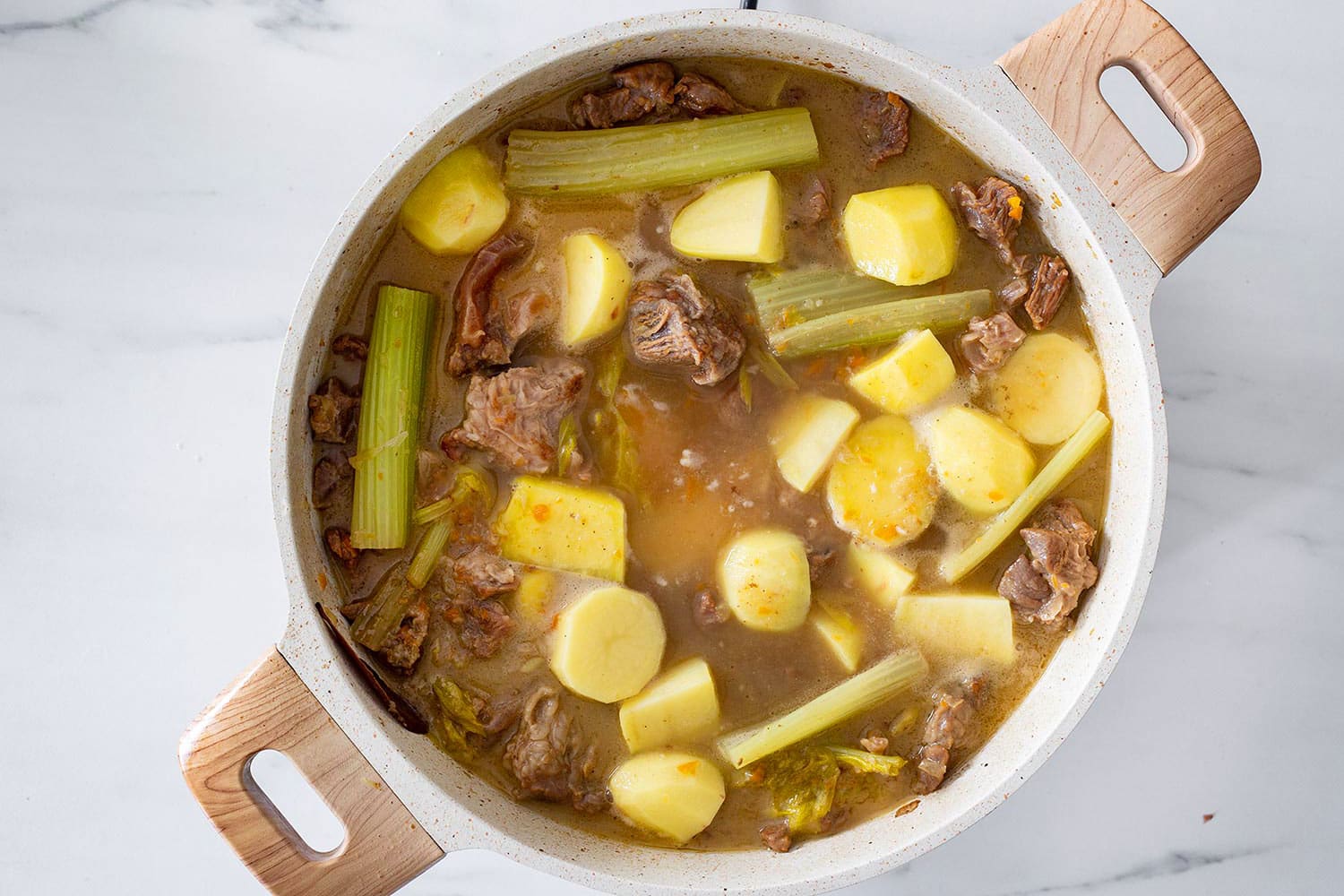 Celery and potatoes cooking with beef in a braising pan.