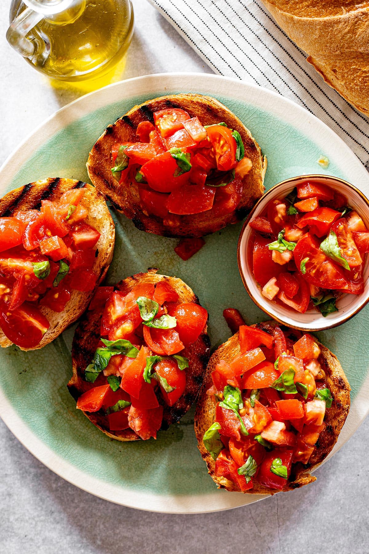 Tomato bruschetta al pomodoro on a turquoise platter with some ingredients on the side.