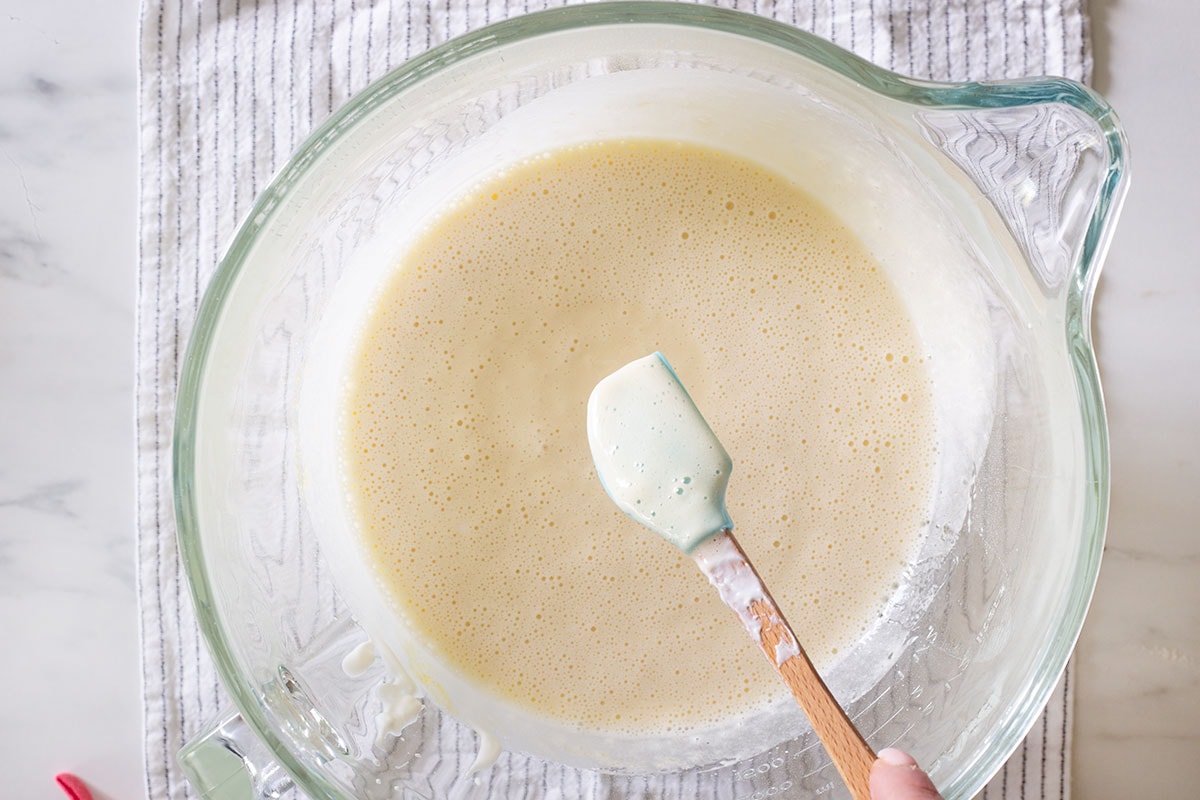 Showing the mixture go eggs, sugar, yogurt, and oil, with a small spatula.