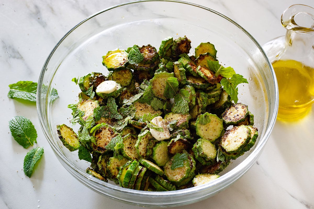 Fried zucchini in a bowl with garlic, seasonings, and mint leaves.