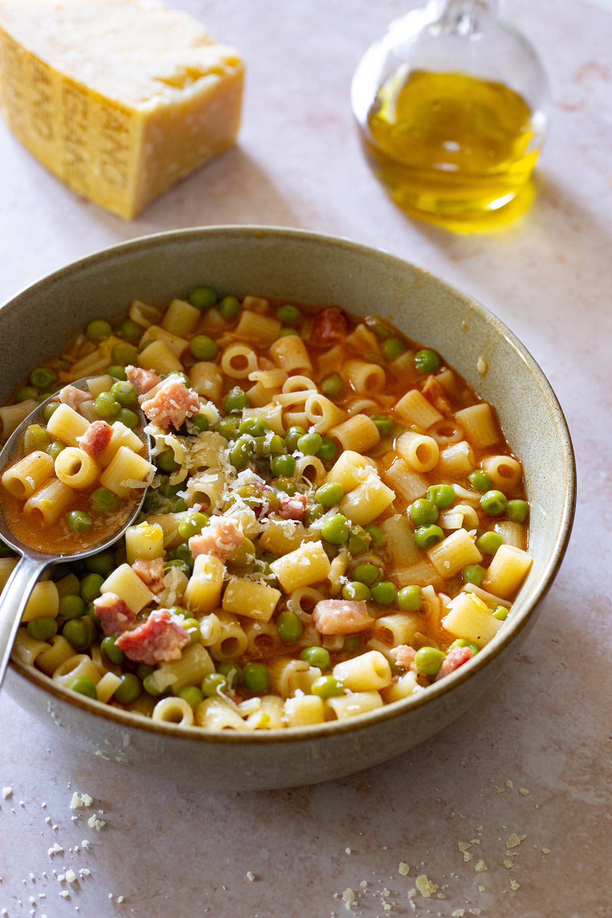 Pasta e piselli in a bowl with a spoon and a parmigiano piece and a bottle with olive oil on the background.