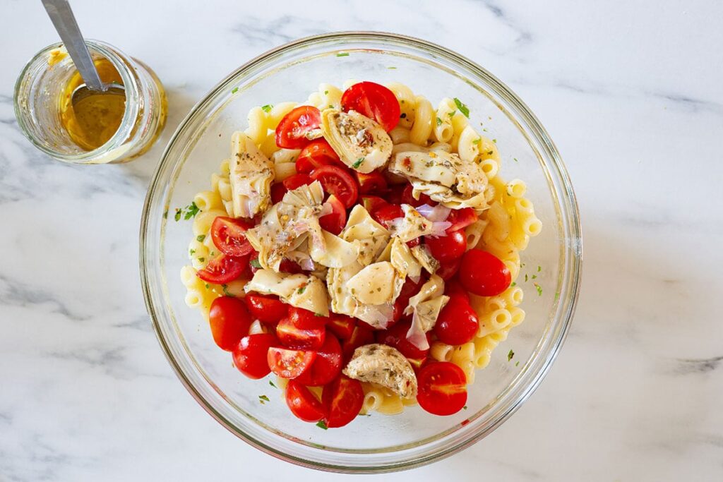 Cherry tomatoes and artichokes added to the bowl with pasta.