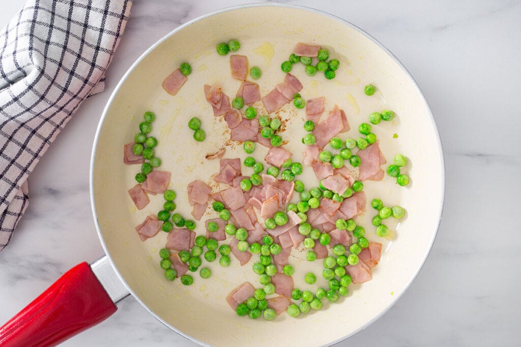 Ham and peans sauteeing in a pan.