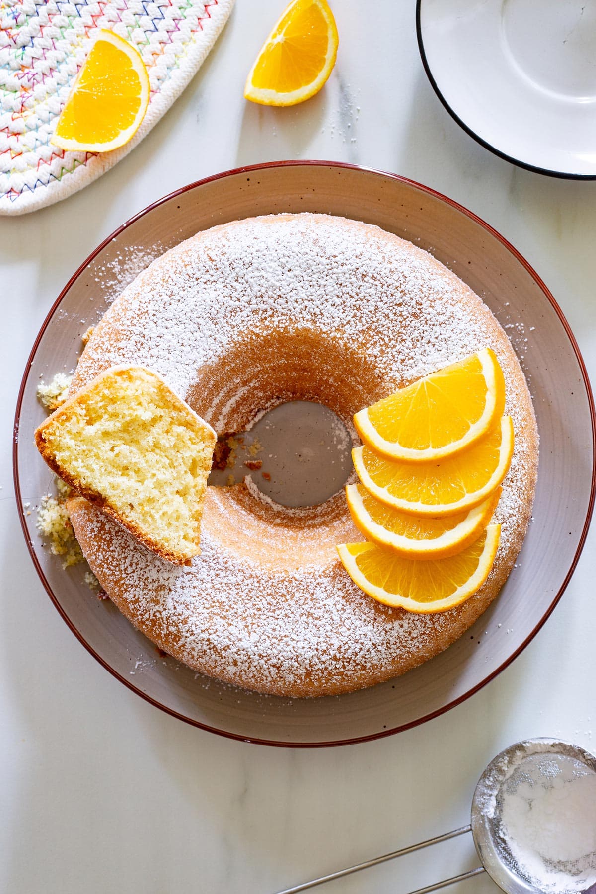 The Ciambella all'arancia cake decorated with fresh orange slices, on a platter.