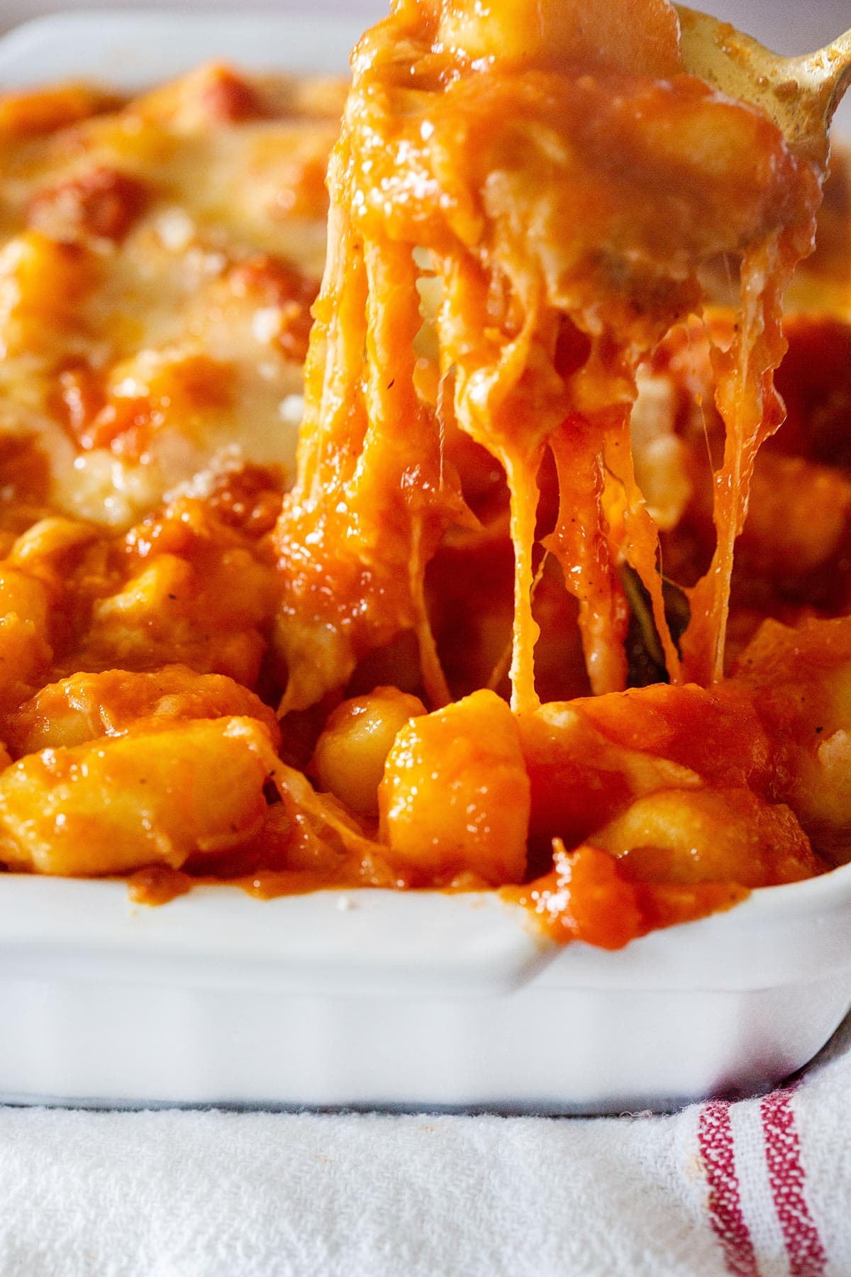 Close-up of the gooey cheese while taking gnocchi from the baking dish.