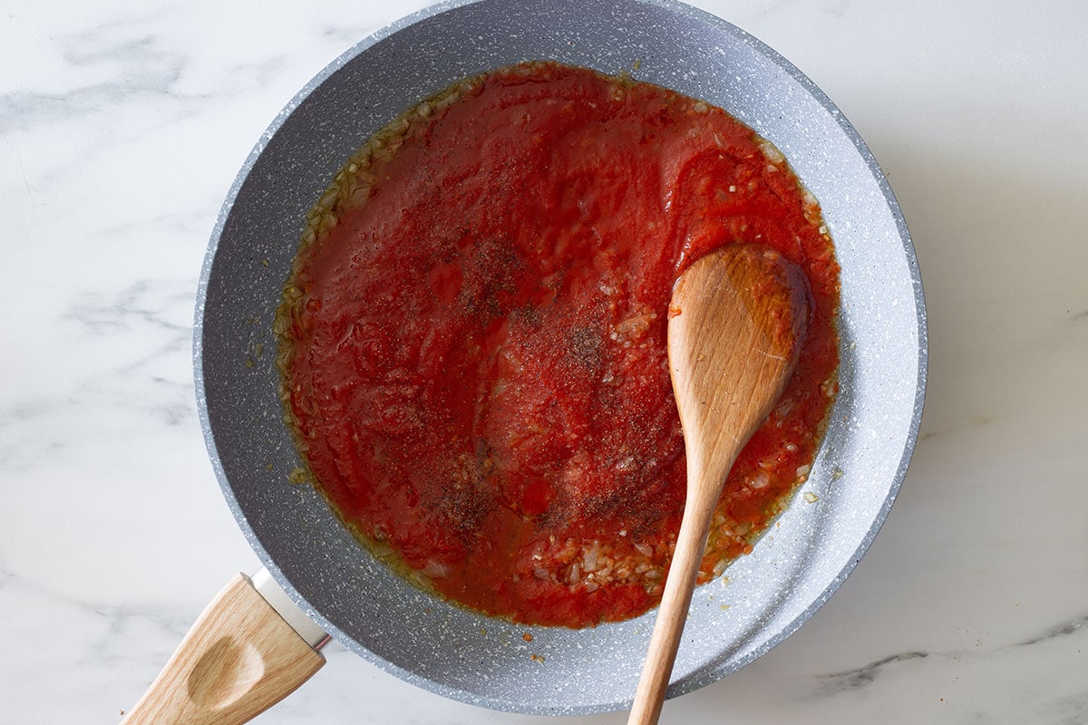 Tomato sauce with onion and seasonings on a pan with a wooden spoon.